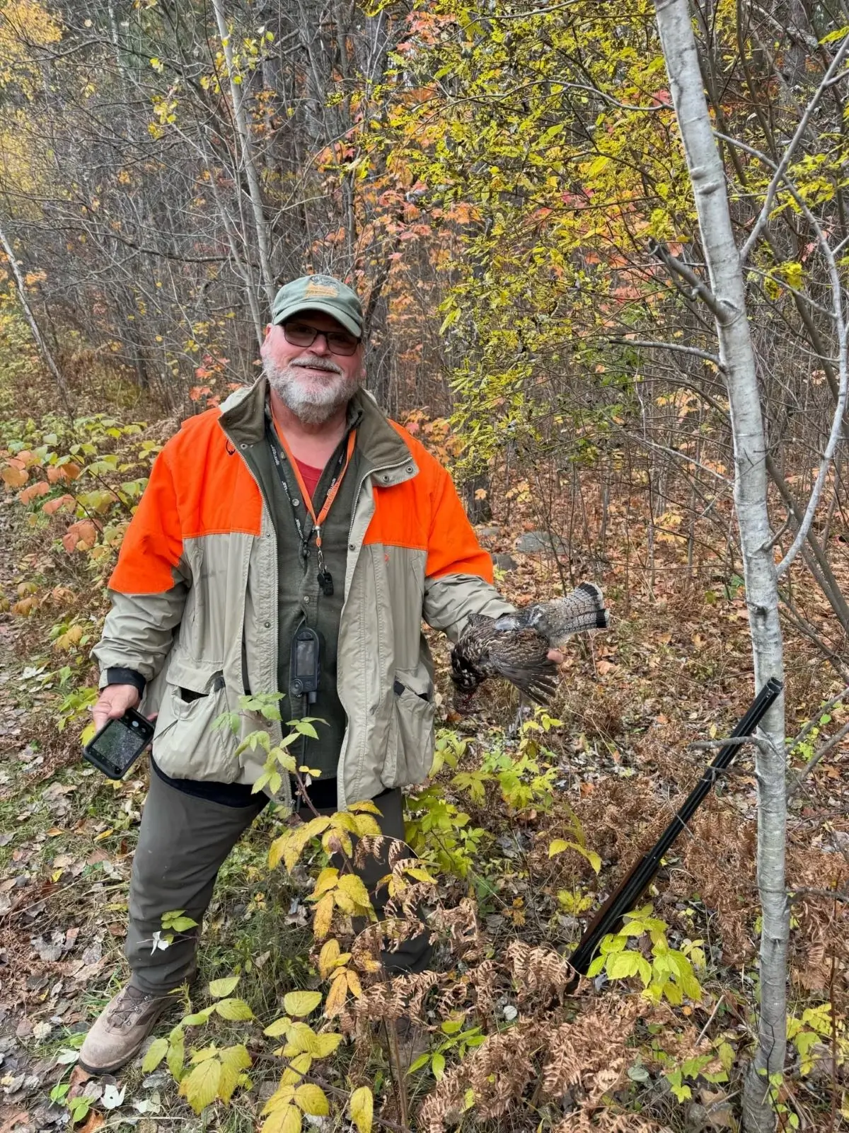 A man in an orange jacket standing next to trees.